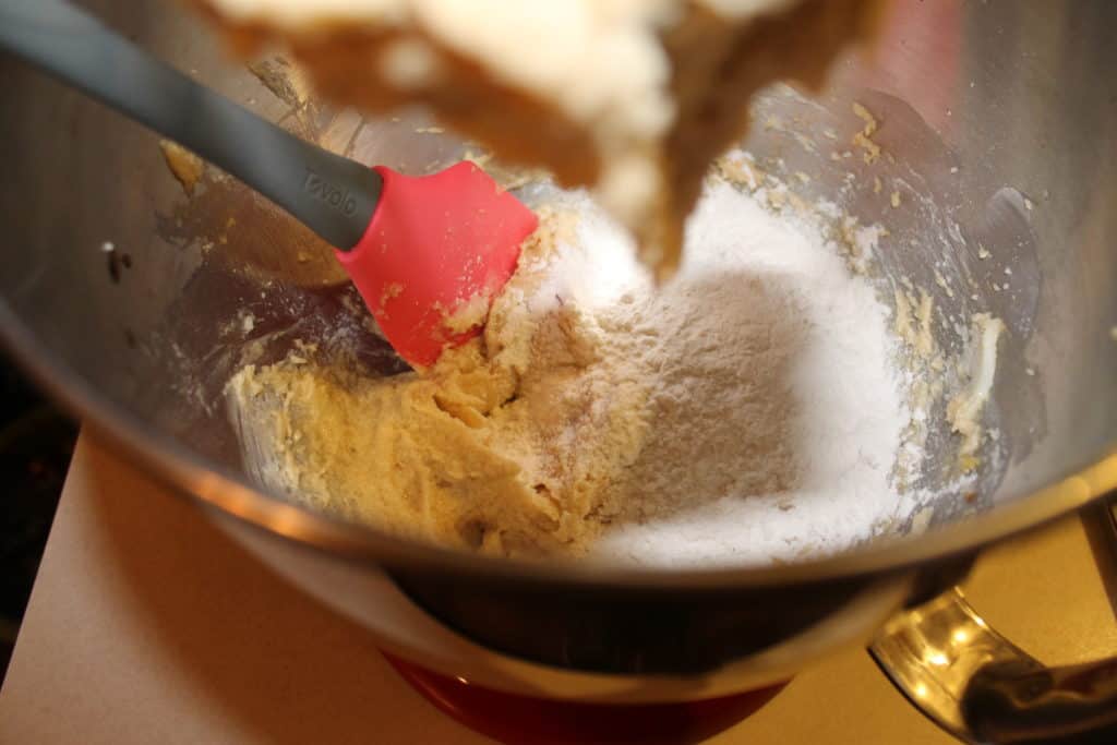 adding flour to the mixing bowl and using a rubber spatula to scrape the sides of the bowl to make sure everything is evenly mixed together