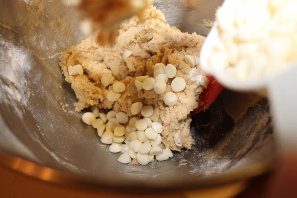 adding white chocolate chips to the cookie dough in the mixing bowl