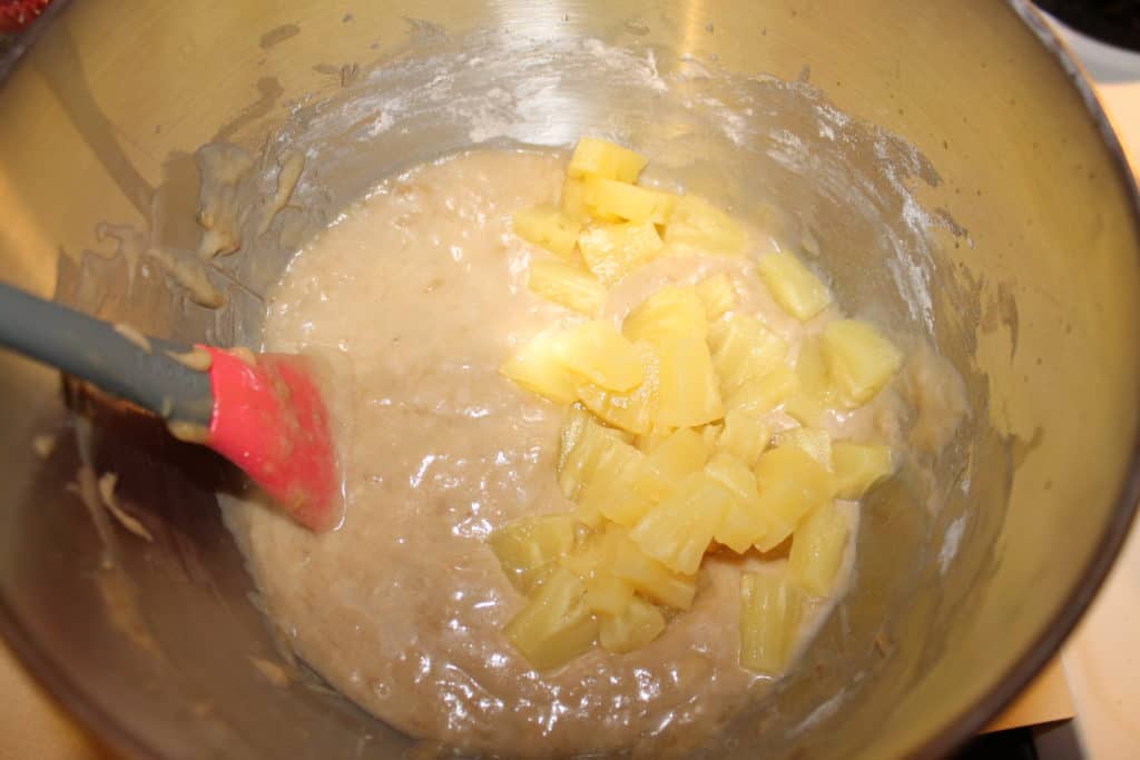 Adding the pineapples to the banana bread batter in the mixing bowl