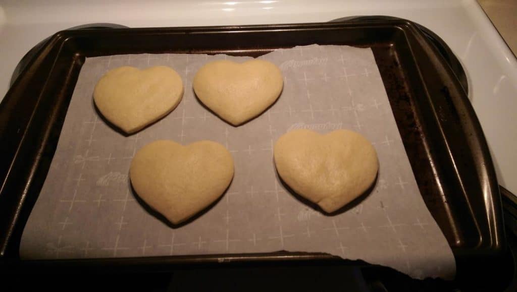 baked heart shaped sugar cookies cooling on the cookie sheet lined with parchment paper