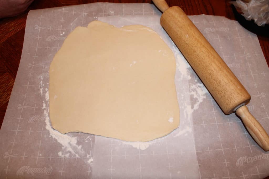 rolled out pie dough on a parchment paper lined with flour and a rolling pin beside it