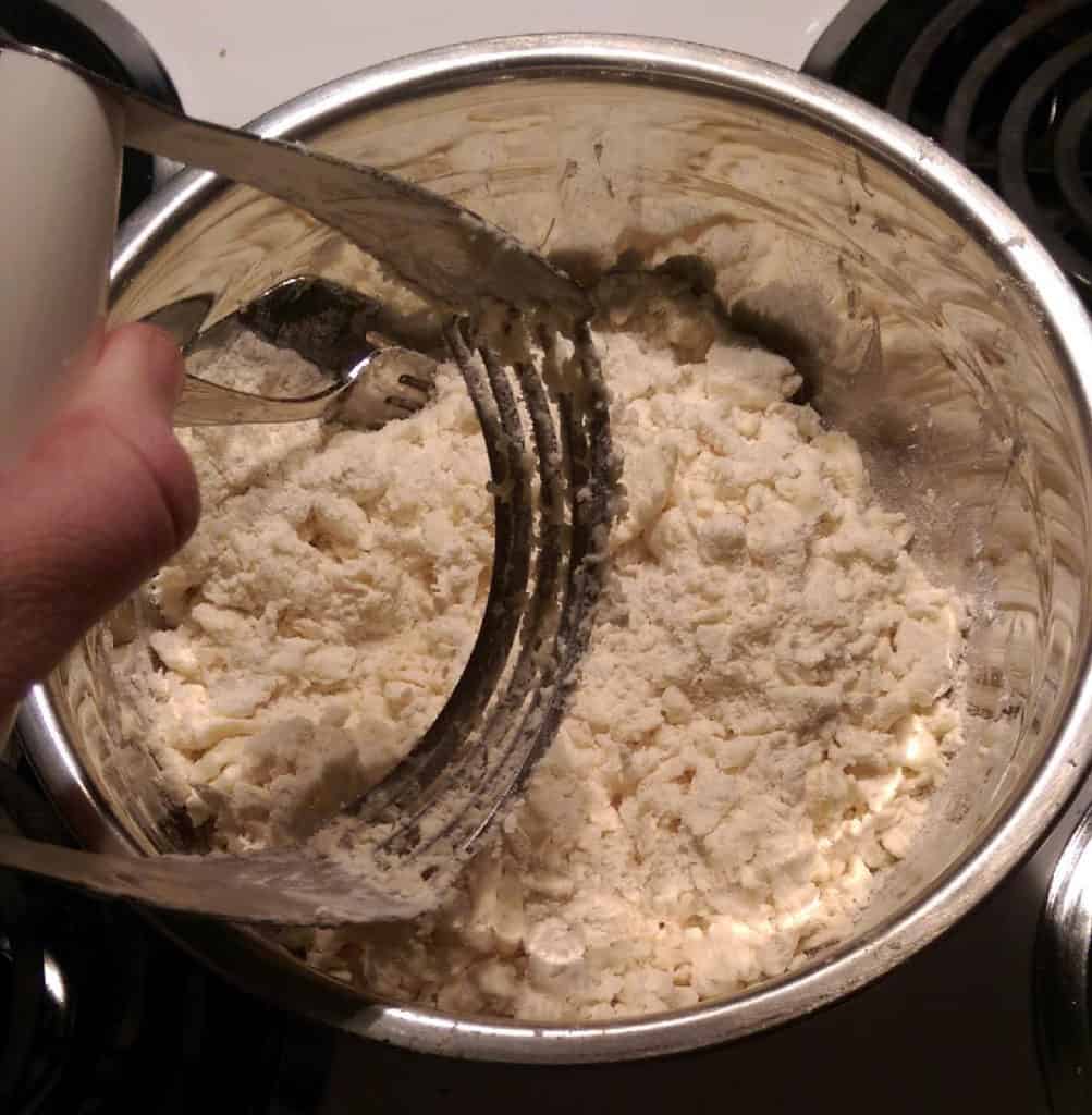 adding flour to the mixing bowl, then using a pastry cutter or two forks to work the flour into the butter and cream cheese