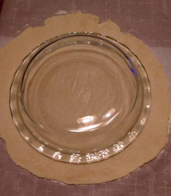 a glass pie dish placed not the rolled out pie dough to ensure the dough is rolled out further than the dish is wide