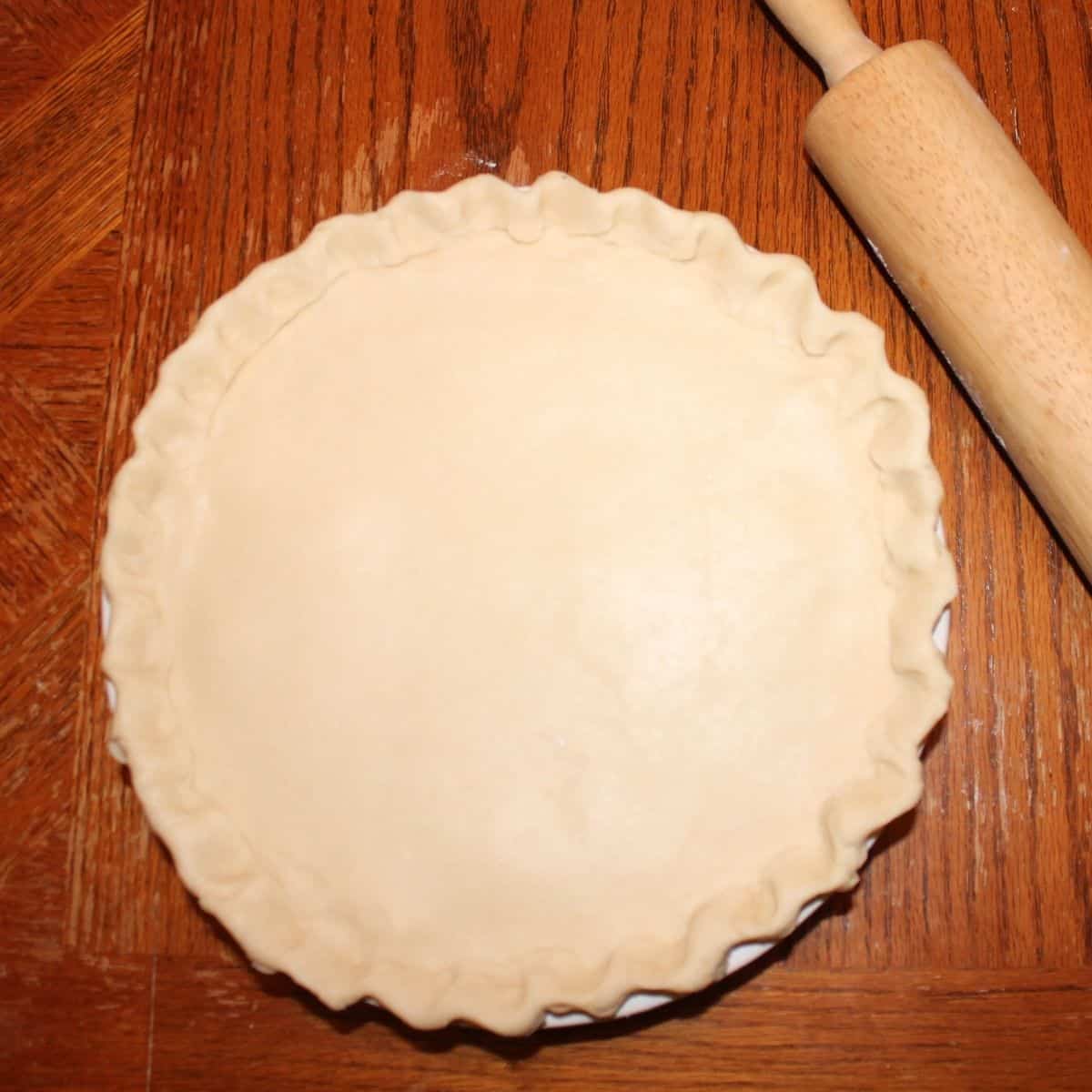 homemade pie crust in a pie pan with a rolling pin beside it