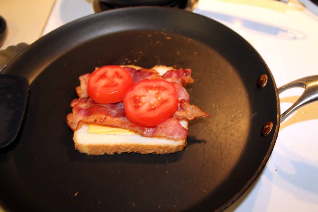 Adding the bacon and tomatoes to the grilled cheese.