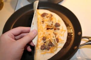 folding the tortilla in half to make a quesadilla in the frying pan