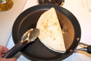 using tongs to flip the quesadilla over to cook both sides