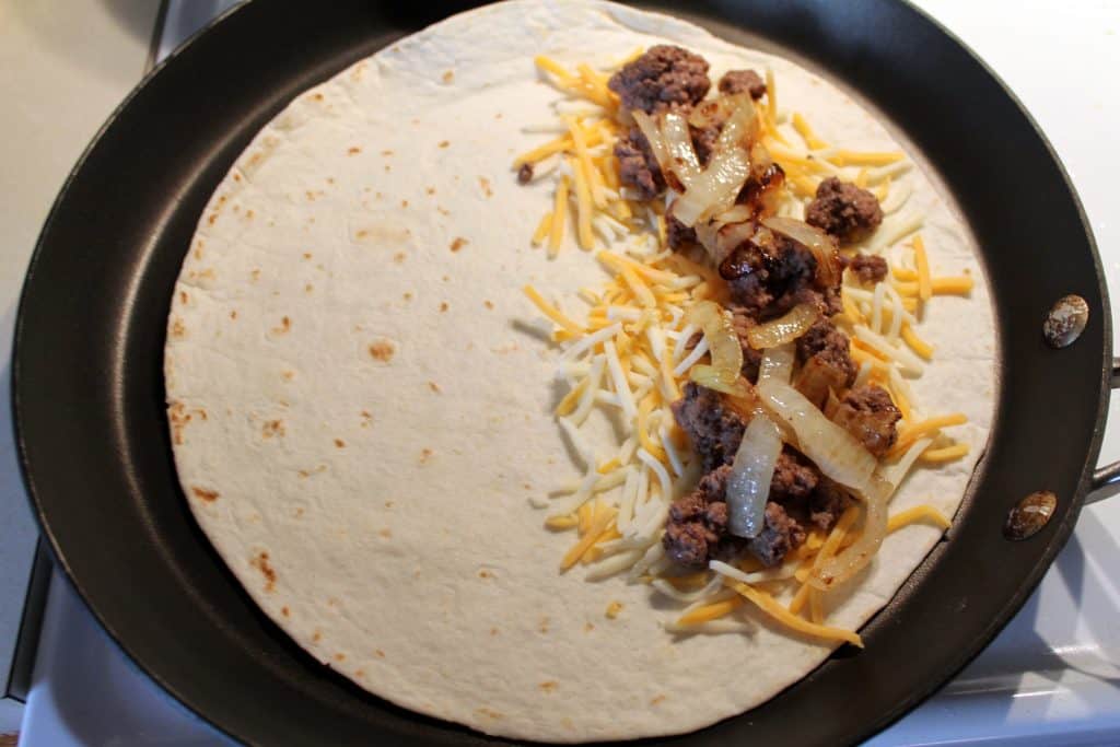 a large frying pan with a tortilla in it filled with cheese hamburger and onions