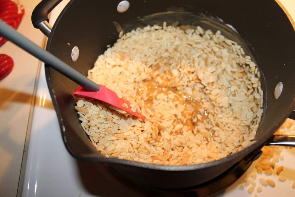 Adding rice crispy cereal to the creamy peanut butter mixture using a rubber spatula to mix