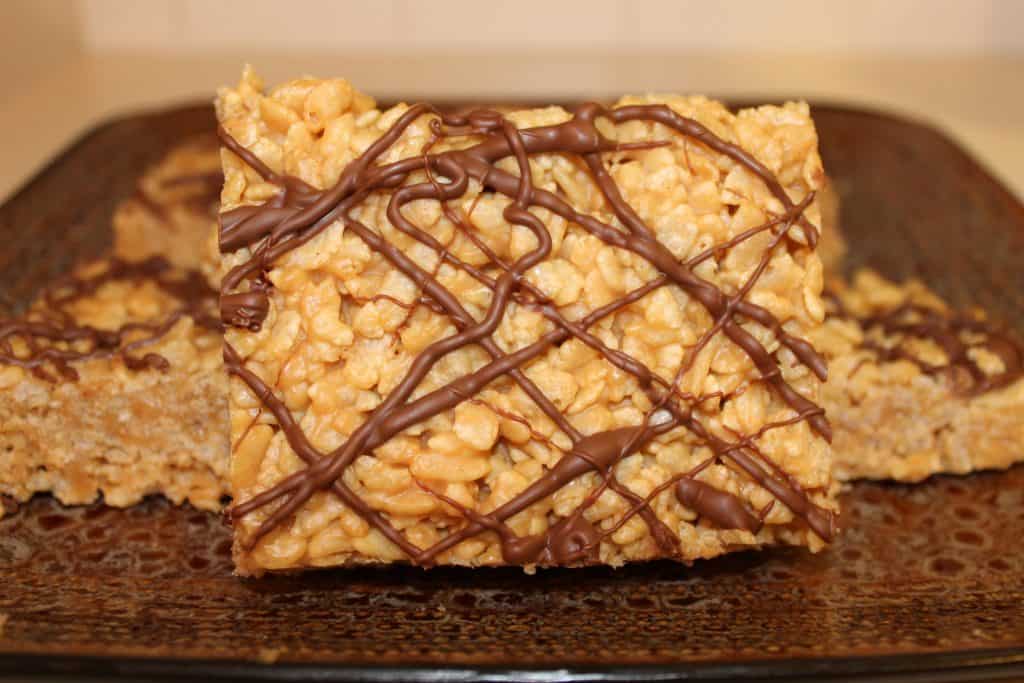 One peanut butter rice crispy treat stood up to show detail on a brown plate.