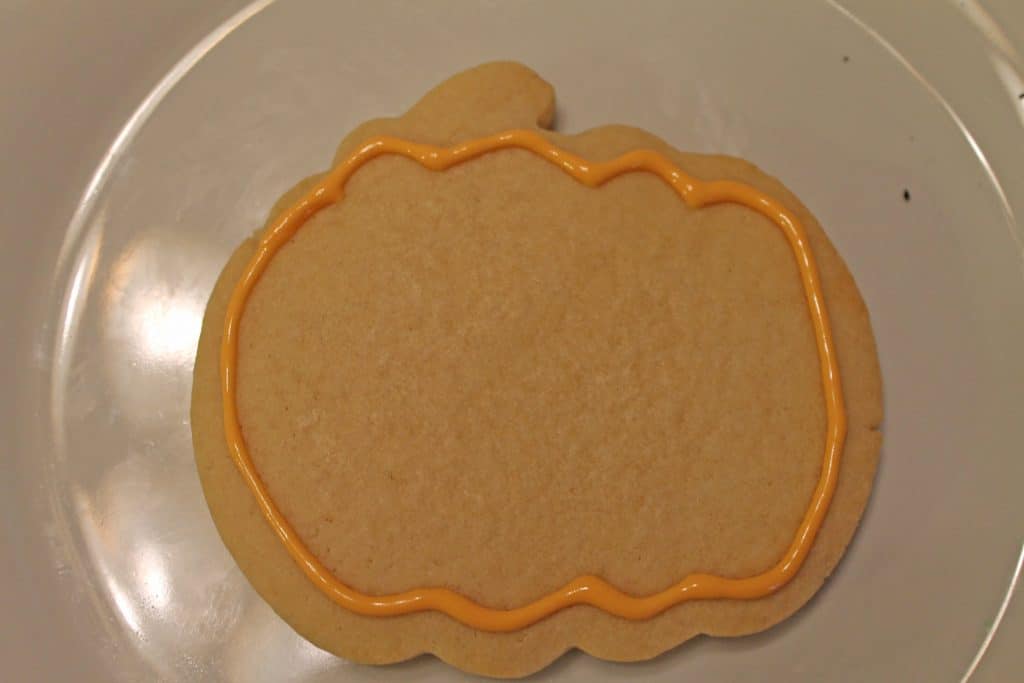 Pumpkin cookie outlined with orange royal icing.