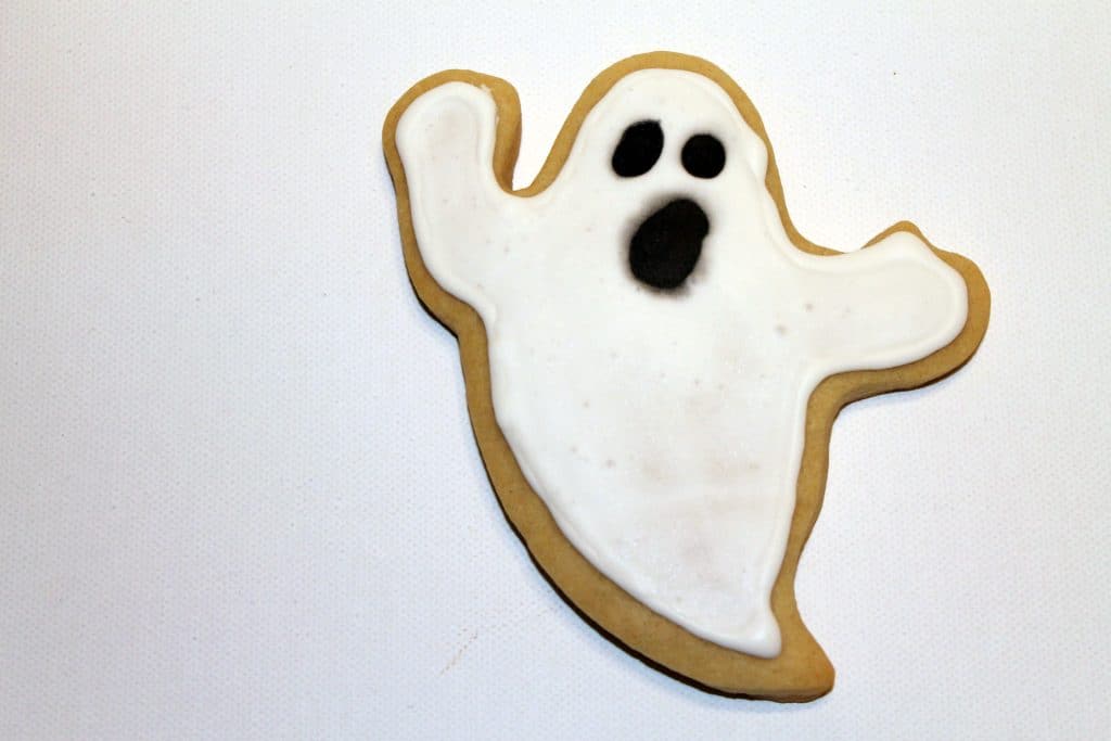 Finished ghost cookie decorated with black eyes and black mouth.