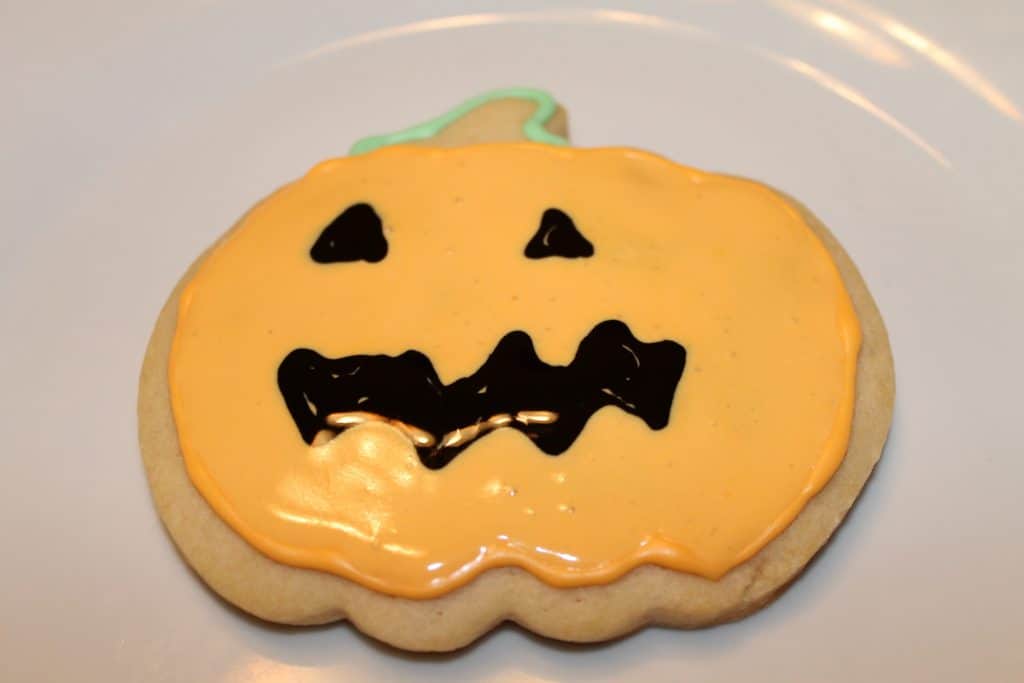 Jack o lantern face with black royal icing using wet on wet technique.