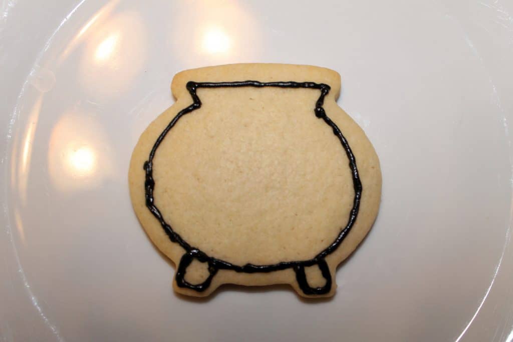 Cauldron cookie outlined in black royal icing.
