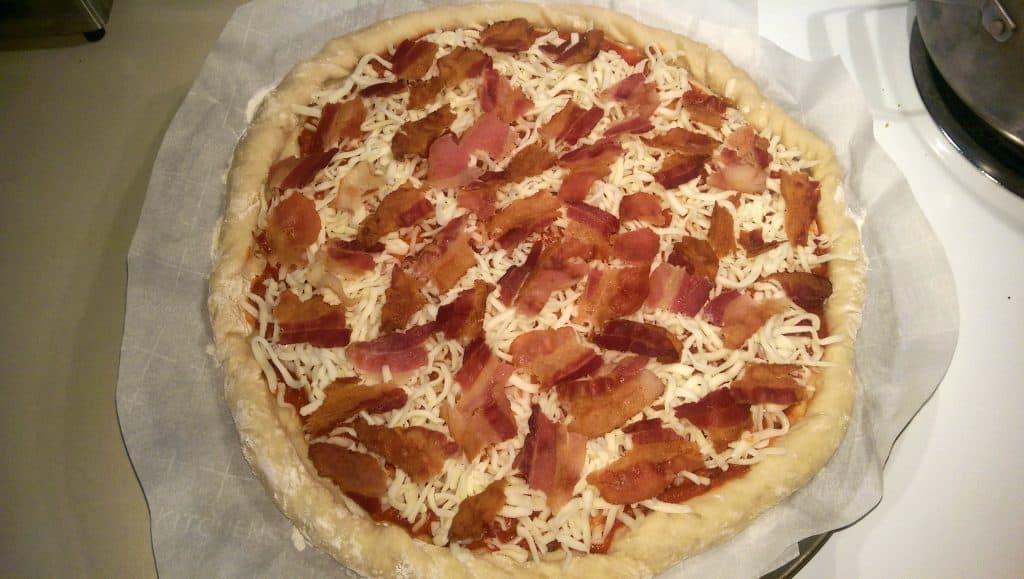 assembling the bacon pizza by adding the sauce than the cheese than the bacon