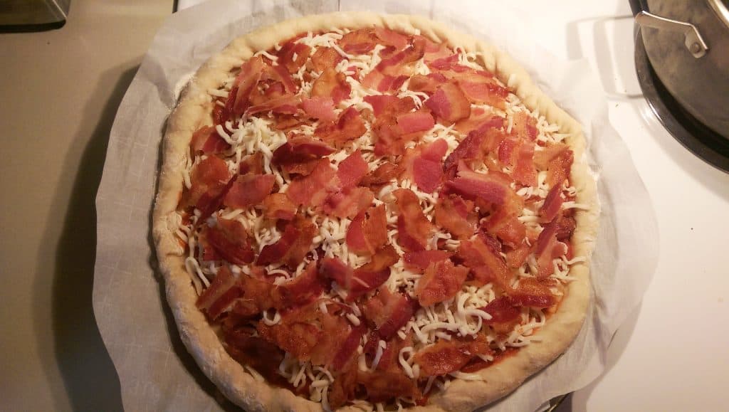 adding a second layer of cheese and bacon to the pizza