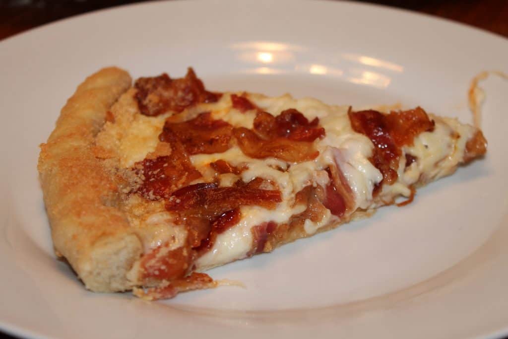 a slice of bacon and cheese pizza on a plate