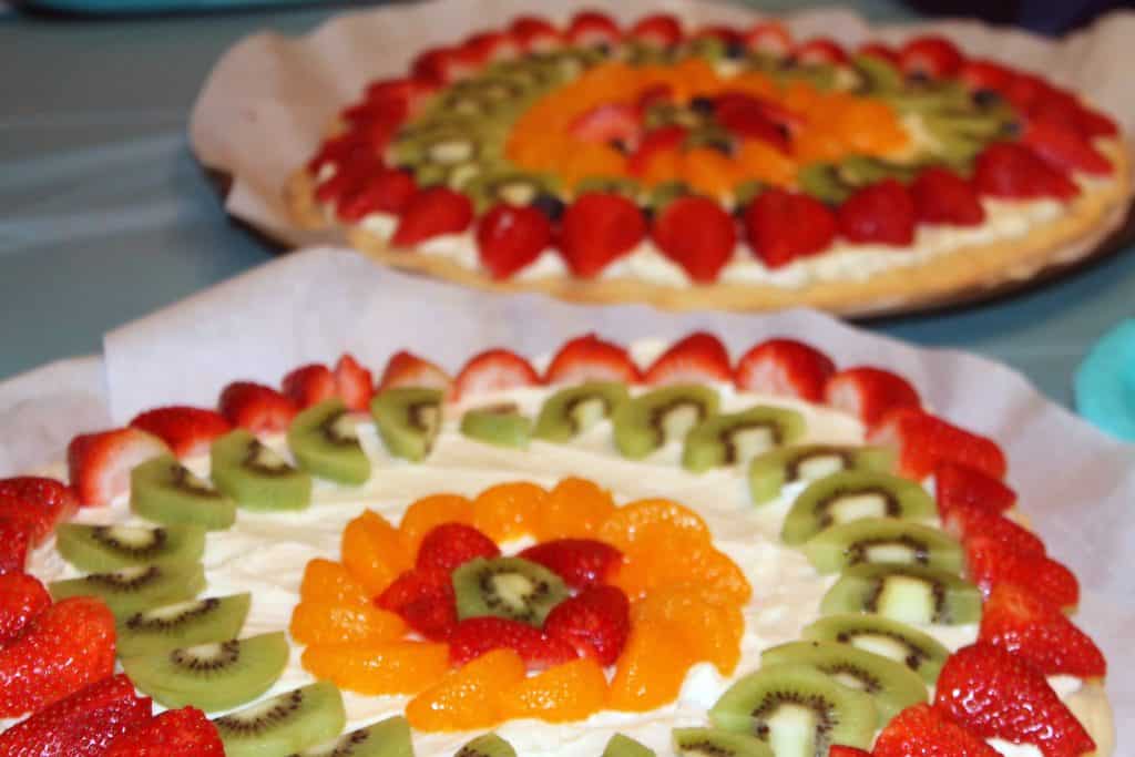 2 fruit pizzas decorated with cream cheese icing strawberries, kiwis and oranges