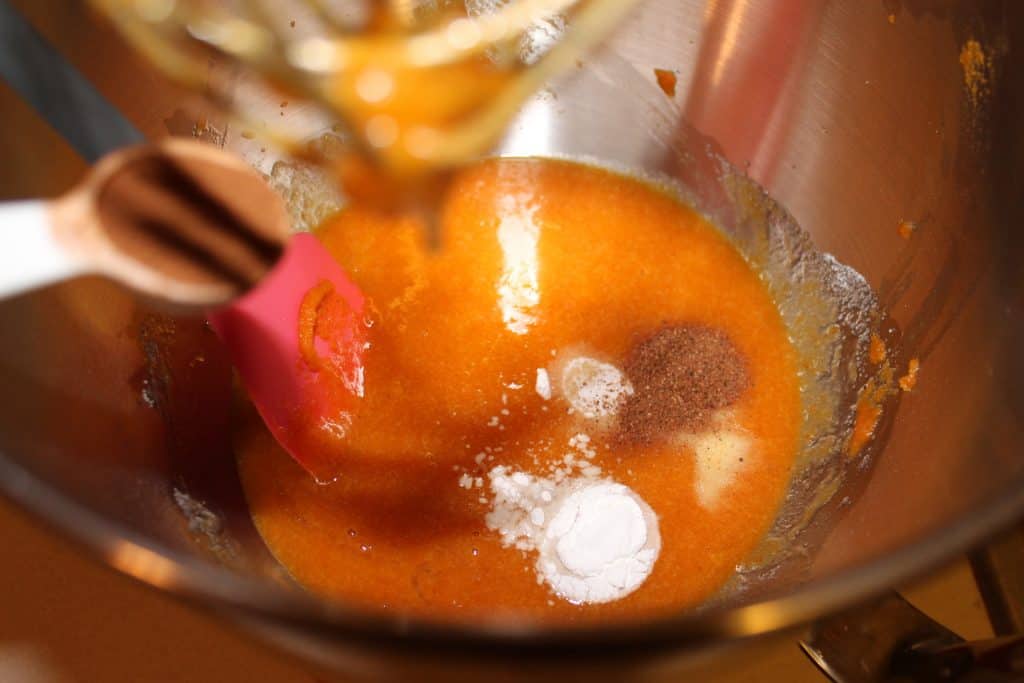 adding spices, baking soda and powder to the pumpkin mixture in the mixing bowl