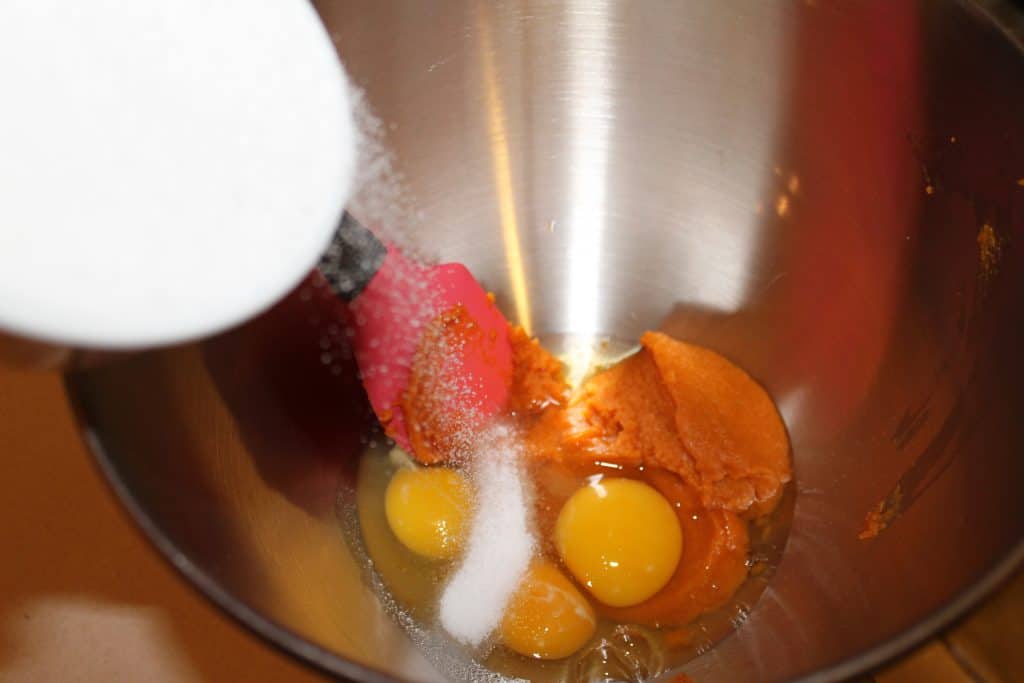 adding sugar, pumpkin puree and eggs to a mixing bowl