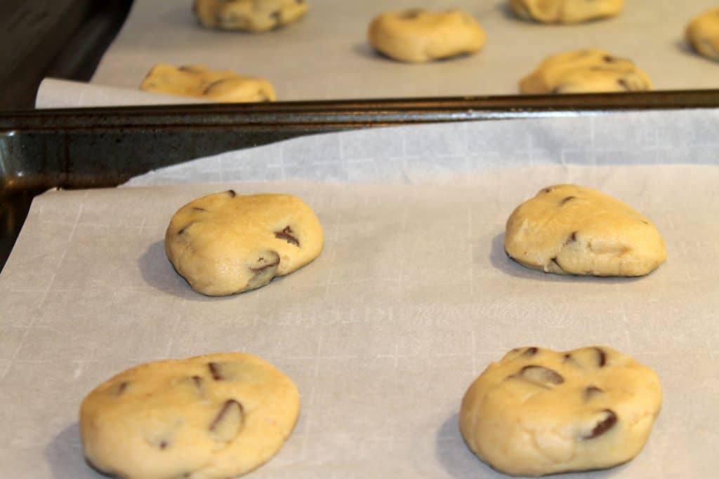 rolled out balls of chocolate chunk cookies on a cookie sheet lined with parchment paper that have been flattened slightly to allow for even cooking
