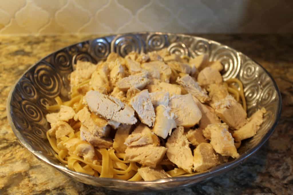 adding sliced chicken to the noodles in the serving bowl