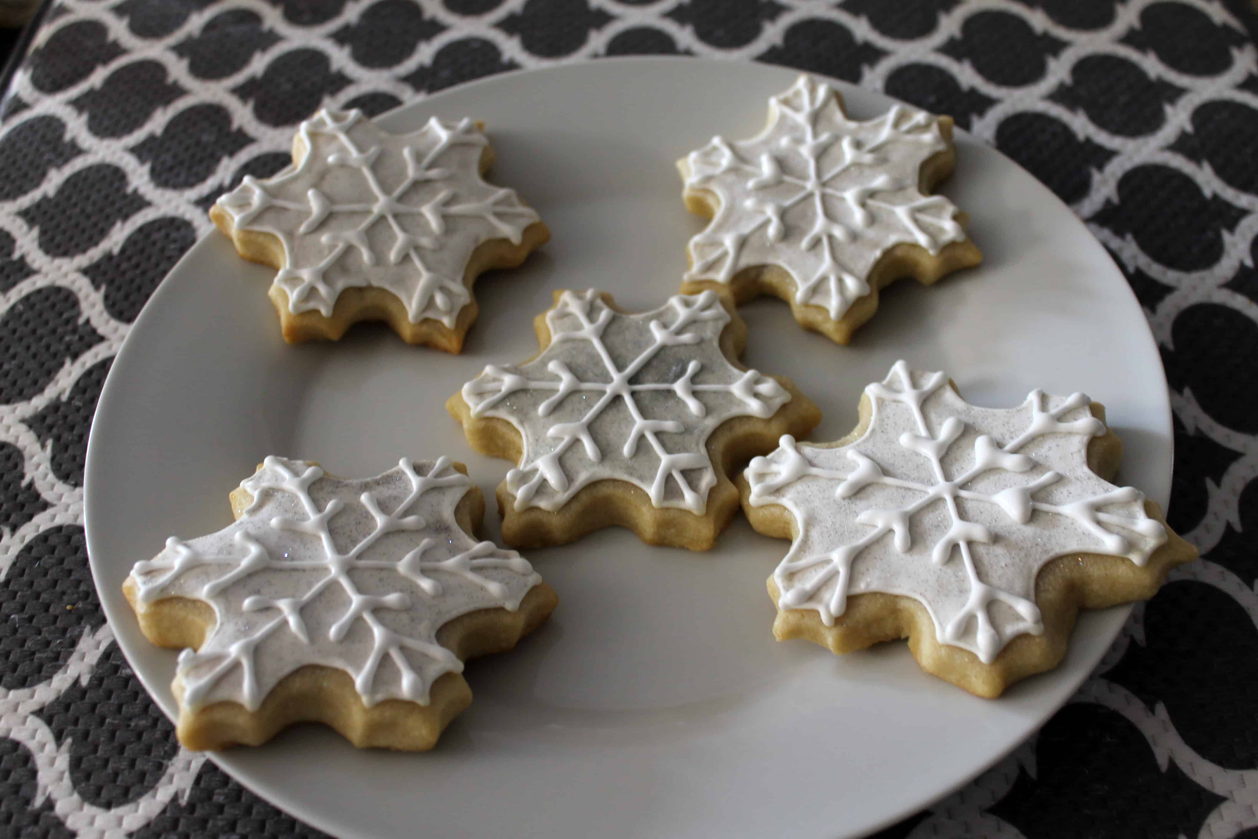 Five snowflake cookies decorated and on a plate.