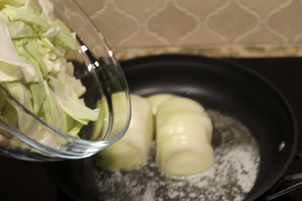 Chopped onions and cabbage in a frying pan.