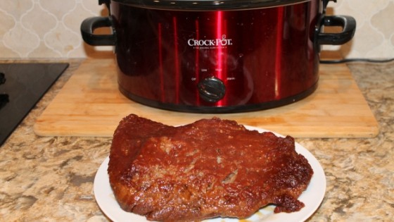 bbq brisket on a plate in front of the slow cooker that was used to cook it