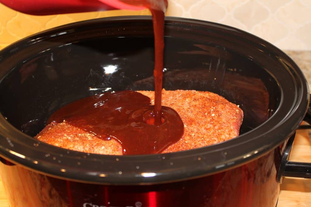 Pouring the barbecue sauce evenly over the brisket in the crockpot.