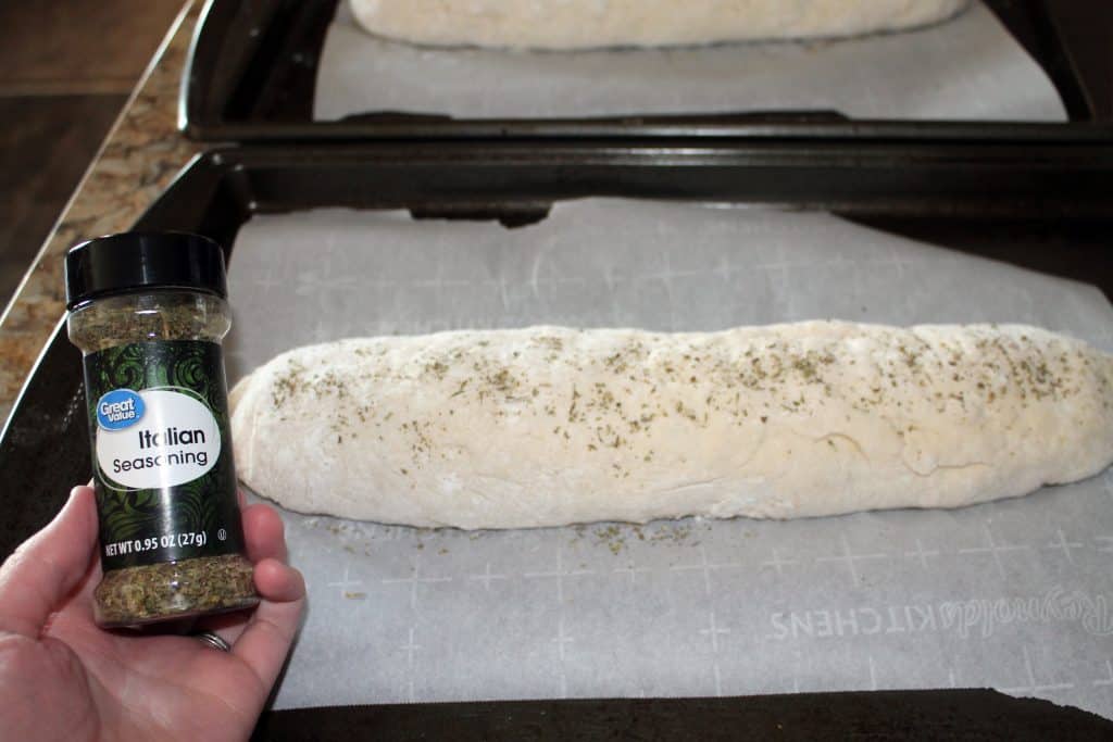Sprinkling italian seasoning onto formed bread loaf.