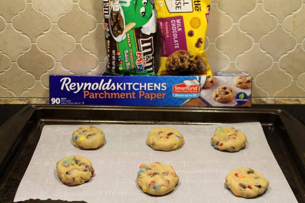 Unbaked chocolate chip m&m cookies on a cookie sheet lined with parchment paper