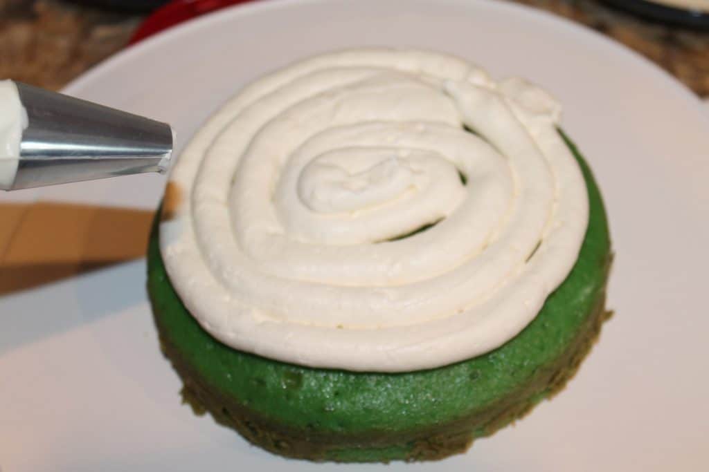 Piping icing onto the first layer of the green cake.