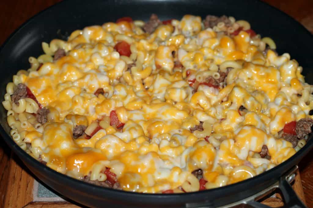 Cheese melted on top of goulash in a frying pan.