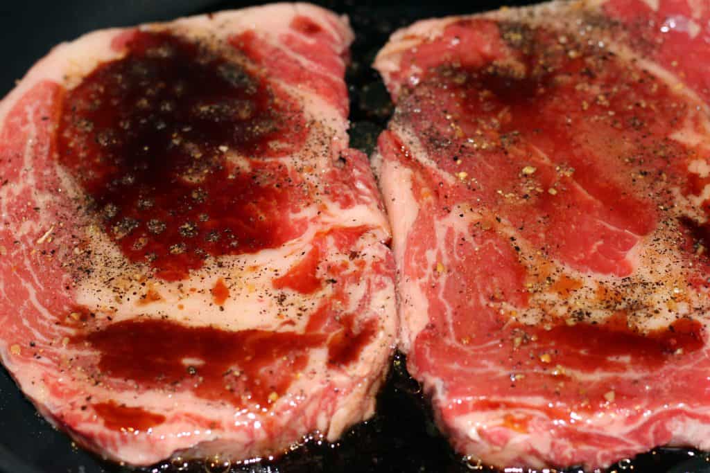 Soy sauce and Worcestershire sauce added on top of steak in frying pan