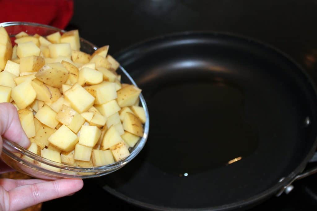 Adding the diced potatoes to the frying pan.