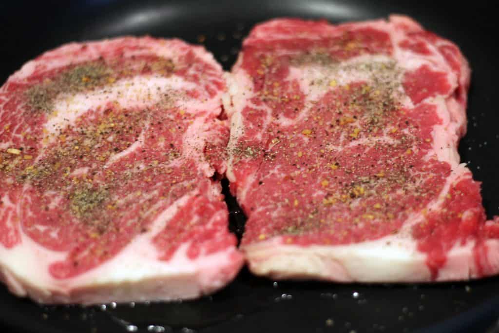 Adding salt, ground pepper, and Montreal seasoning to the steak