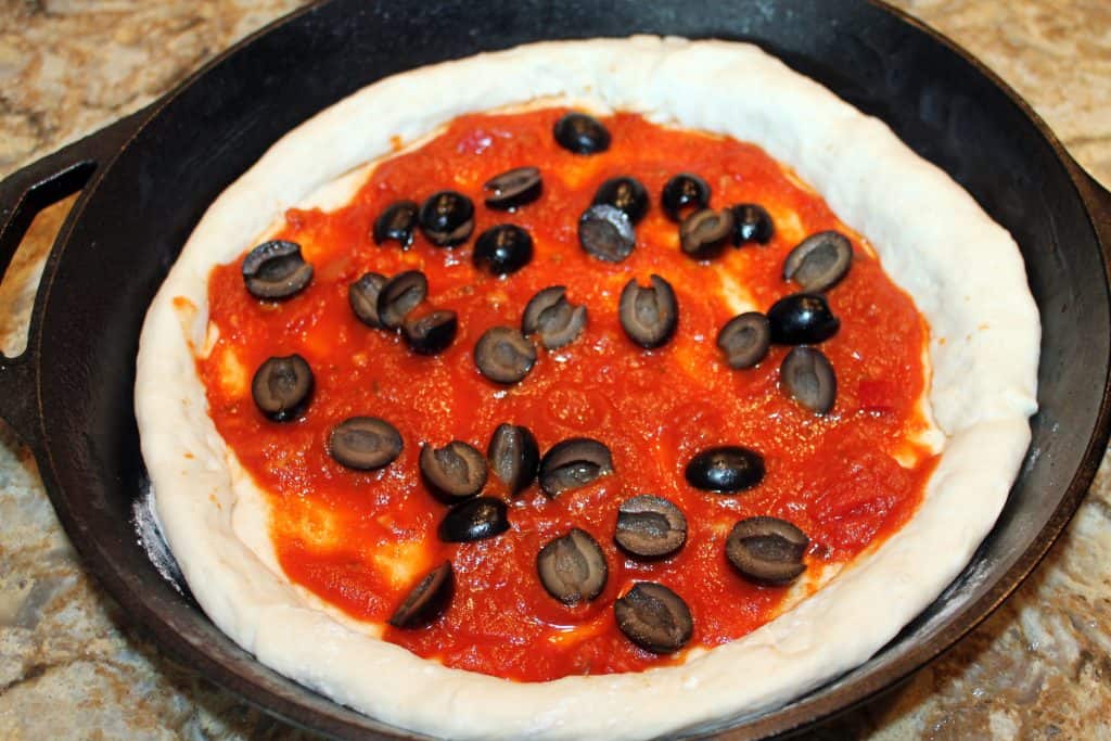 Pizza sauce and black olives on pizza dough