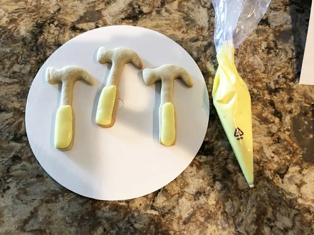 Decorating the hammer shaped cookie with yellow icing