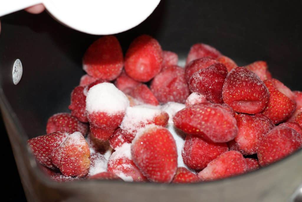 frozen strawberries and granulated sugar added into a saucepan