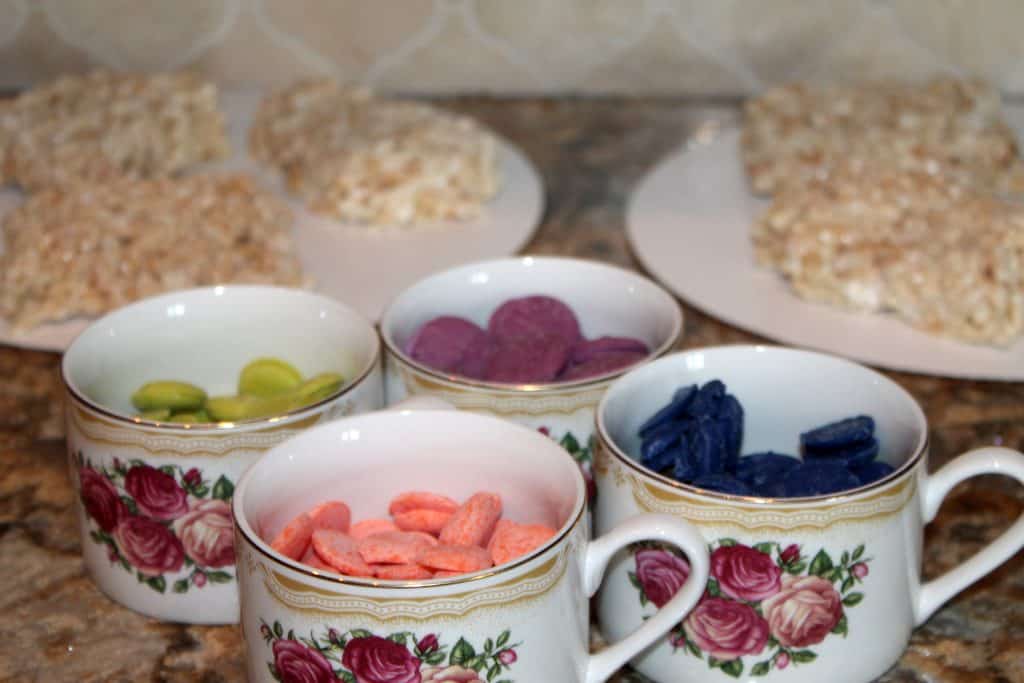 Rice crispy treats cut into squares and also showing the green, blue, orange and purple candy melts