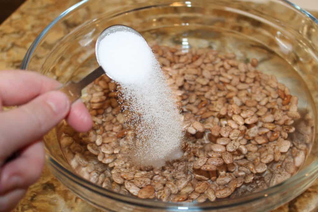 large bowl of dried pinto beans with water and salt being added