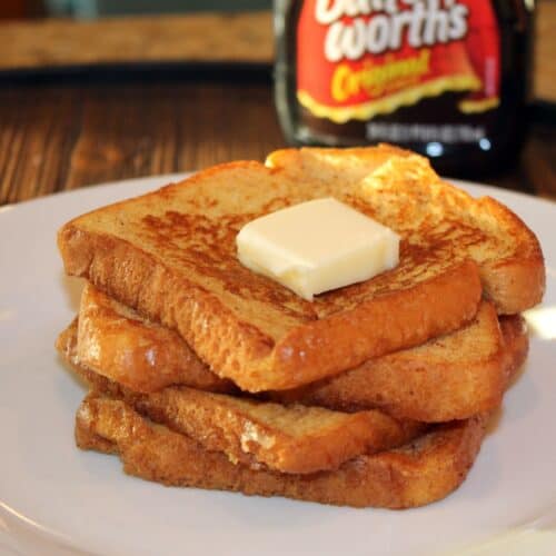four french toasts stacked on a play with butter and syrup in the background
