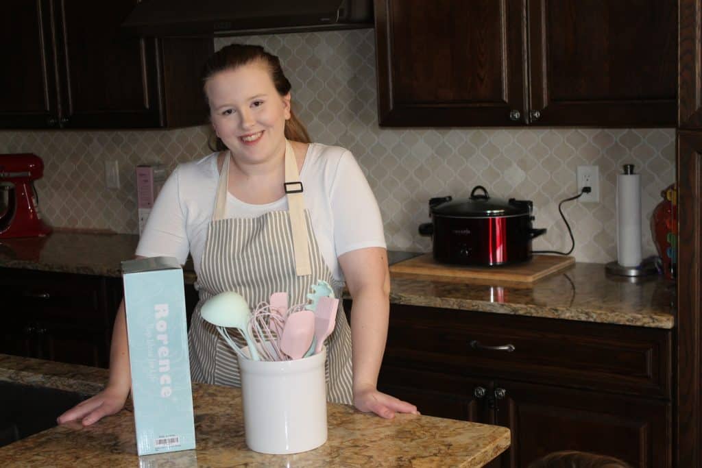 a woman wearing an apron standing by some Rorence kitchen utensils