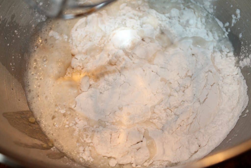 adding flour to the mixing bowl with the yeast mixture