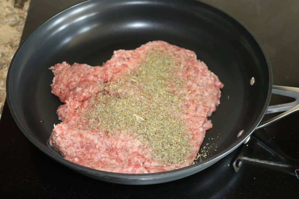 a large frying pan with ground beef an Italian seasoning on top