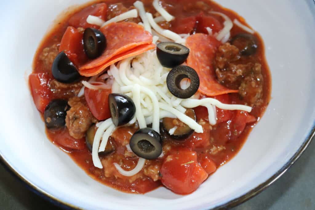 a bowl with pizza soup topped with mozzarella cheese olives and pepperonis