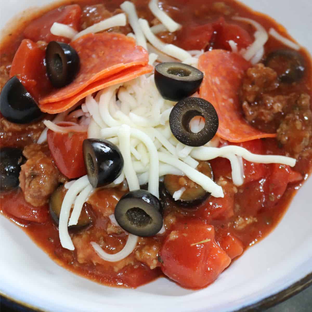 a bowl of pepperoni pizza soup with cheese black olives and tomatoes