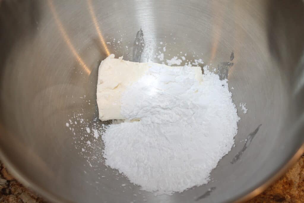a mixing bowl with cream cheese and powdered sugar in it
