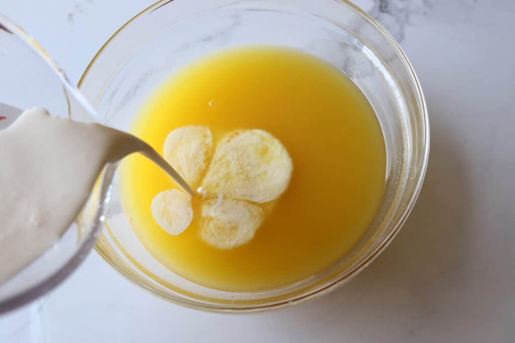Pouring cream into the juice in the glass bowl.